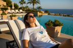 Woman relaxing on a lounge chair by a pool with ocean view